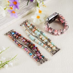 May include: Beaded Apple Watch bands in various colors, including pink, blue, and brown. The bands feature multiple strands of round beads and silver-toned connectors. One band is attached to a silver Apple Watch.