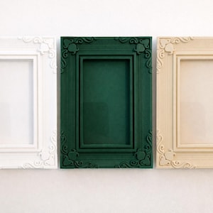 May include: Three rectangular picture frames in white, dark green, and cream. Each frame has an ornate, decorative border with scrolled details. The frames are empty, ready for photos or artwork.