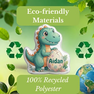 May include: A green and orange dinosaur holding a speckled egg with the name "Aidan" on it. The image includes text that reads "Eco-friendly Materials" and "100% Recycled Polyester". The background features green leaves and recycling symbols.