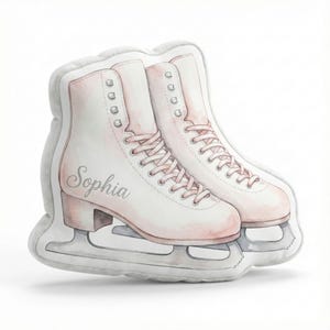 May include: A pair of decorative ice skates in a soft, watercolor style. The skates are primarily white with pale pink accents, including the laces and heel. The name "Sophia" is written on one skate. The blades are silver.
