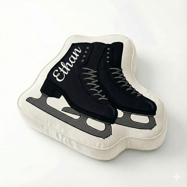 May include: A decorative pillow shaped like a pair of black ice skates. The skates have gray blades and white laces. The name "Ethan" is written in white script on one skate. The pillow is off-white.