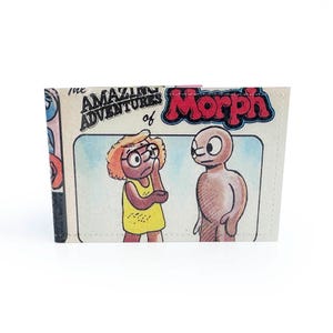 May include: A folded wallet with a cartoon illustration from "The Amazing Adventures of Morph." The design features two characters, one with glasses and a yellow dress, and the other a brown figure. The word "Morph" is in red.