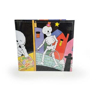 May include: A black wallet featuring a colourful illustration of a skeleton walking a dog on a city street. The skeleton wears a top hat and the dog is white. The background features buildings in shades of purple, red, and yellow.