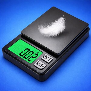 May include: A black digital scale with a green LED display showing 0.002 g. A white feather rests on the scale's surface. The scale has two buttons labeled "/T" and "M/P". The background is a solid blue.