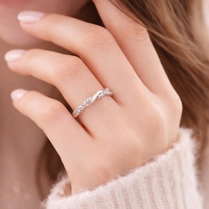 May include: A silver ring with a twisted design, adorned with small, sparkling stones. The ring is worn on a finger, showcasing its delicate and elegant appearance. The ring's design is a continuous, flowing pattern.