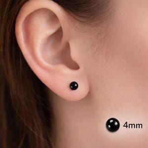 May include: A close-up of a person's ear with a small, round, black stud earring. A loose earring of the same style is shown with the text "4mm" next to it, indicating the size of the earring.