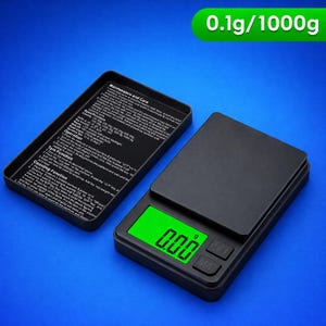 May include: A black digital pocket scale with a green illuminated display showing "0.00 g". The scale has two buttons and a removable lid with printed instructions. The text "0.1g/1000g" is in a green rectangle.