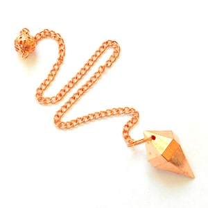 May include: A copper-colored pendulum with a faceted, pointed design, connected to a chain and a decorative ball. The chain and ball have a matching copper tone, set against a white background.