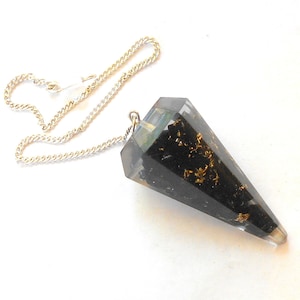 May include: Black and gold crystal pendulum with a silver chain. The pendulum is shaped like a cone and has gold flecks embedded in the black crystal.