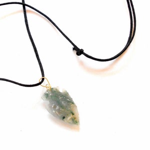 Puede incluir: Un colgante de punta de flecha de ágata verde y blanca en un collar de cordón negro.