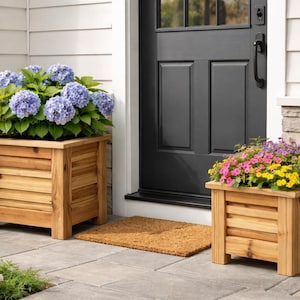 May include: Two wooden planters filled with colorful flowers sit on a patio. One planter holds blue hydrangeas, the other has a mix of pink, yellow, and purple blooms. The planters are made of light-colored wood.