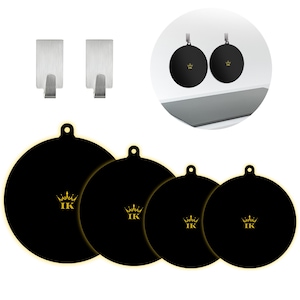 Könnte beinhalten: Vier runde, schwarze Silikondeckel in verschiedenen Größen, jeweils mit einem goldenen Kronenlogo und den Buchstaben IK versehen. Das Set enthält zwei selbstklebende Wandhaken aus gebürstetem Edelstahl, dargestellt in einem runden Inset.