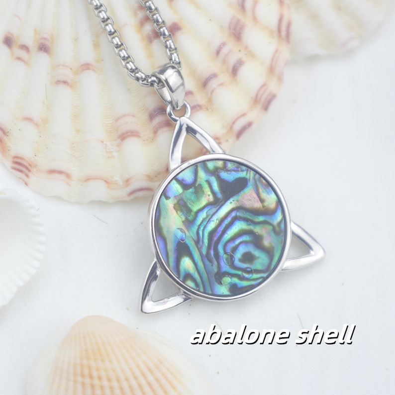 May include: A silver-toned pendant necklace featuring a circular inlay of iridescent abalone shell set within a triangular metal frame. The pendant hangs from a box chain. The text "abalone shell" is printed in the lower right corner.