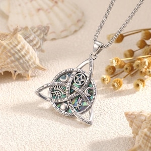 May include: A silver-toned pendant necklace featuring a triangular frame with an iridescent abalone shell inlay. The metal surface is engraved with symbols including a pentagram, crescent moon, and eye, alongside text reading Speak With Love.