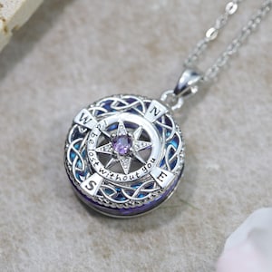 May include: A silver-toned circular pendant necklace featuring a compass design with a central purple stone. The outer ring displays the letters N, S, E, W and the engraved text "I be lost without you" surrounded by intricate metal knotwork patterns.