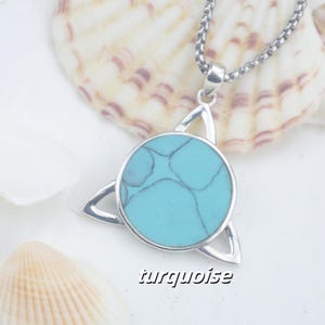 May include: A silver-toned pendant necklace featuring a circular turquoise stone with dark veining, set within a triangular metal frame. The pendant hangs from a silver-toned box chain. The word turquoise is printed in black text at the bottom.