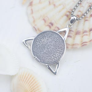 May include: A silver-coloured pendant necklace featuring a circular centre with a textured, intricate pattern surrounded by a triangular frame. The metal is stamped with S925, indicating sterling silver composition, and hangs from a box chain.