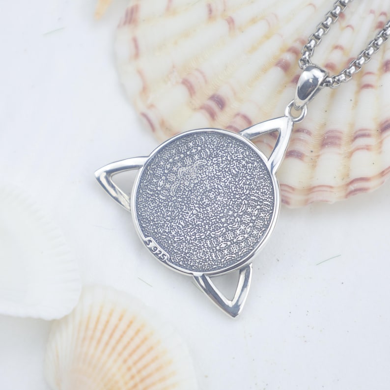 May include: A silver-coloured pendant necklace featuring a circular centre with a textured, intricate pattern surrounded by a triangular frame. The metal is stamped with S925, indicating sterling silver composition, and hangs from a box chain.