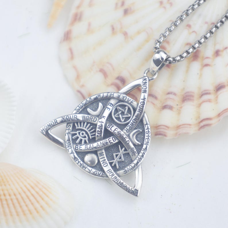 May include: A silver-toned metal pendant necklace featuring a triquetra knot design. The circular centre displays engraved symbols including a pentagram, crescent moon, eye, and rune, with text reading "KNOW YOUR POWER," "BE KIND," and "BE BALANCED."