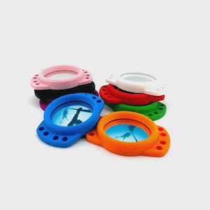 May include: A selection of colourful, round silicone cases with a circular mirror. The cases are in various colours, including blue, orange, pink, white, red, green, and black. Each case has a small image of a person underwater. The cases are stacked.