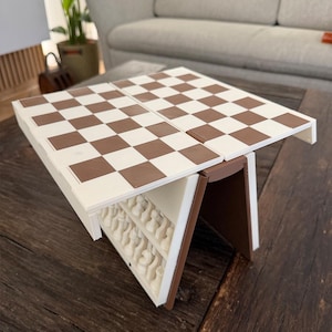 Puede incluir: Un juego de ajedrez plegable marr&oacute;n y blanco, abierto y listo para jugar. El tablero es una cuadr&iacute;cula de cuadrados marrones y blancos alternados. El juego est&aacute; sobre una mesa de madera oscura, con las piezas guardadas dentro.