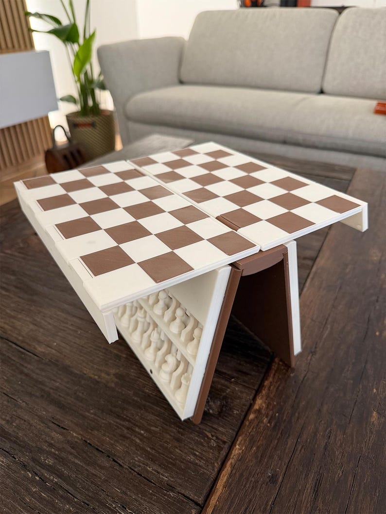 Puede incluir: Un juego de ajedrez plegable marr&oacute;n y blanco, abierto y listo para jugar. El tablero es una cuadr&iacute;cula de cuadrados marrones y blancos alternados. El juego est&aacute; sobre una mesa de madera oscura, con las piezas guardadas dentro.