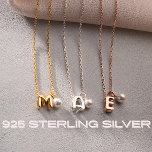 May include: Three necklaces featuring the letters M, A, and E in gold, silver, and rose gold tones, each accented with a small white pearl. The text 925 STERLING SILVER is printed at the bottom of the image, indicating the material of the jewellery.