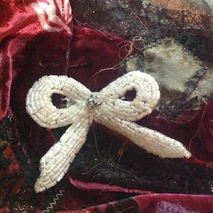 May include: A white beaded bow with a rhinestone centre, resting on a red velvet fabric with black lace accents.