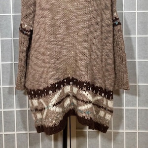 May include: A brown knit sweater with a scoop neck and long sleeves. The sweater has a patterned design at the bottom in shades of brown, white, and teal. A gold-colored chain necklace is around the mannequin's neck.