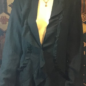 May include: A black blazer with a ruffled neckline and a long sleeve. The blazer is worn over a purple skirt.