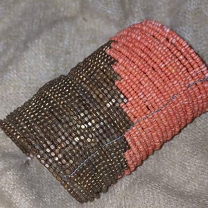 May include: A two-tone beaded bracelet. The bracelet is made up of bronze-coloured beads and coral-coloured beads. The beads are strung together with a thin, silver-coloured wire.