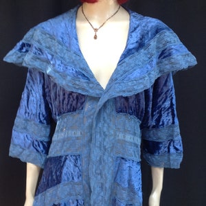 Puede incluir: Una chaqueta de terciopelo azul y encaje con un cuello ancho y un dobladillo alto-bajo. La chaqueta tiene un ajuste holgado y está adornada con delicados detalles de encaje.
