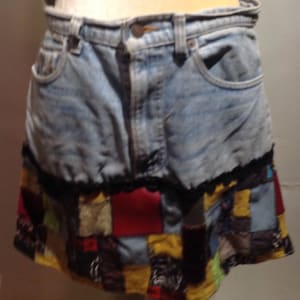May include: A denim skirt with a patchwork hem. The skirt is light blue and has a black lace trim. The patchwork is made of different colored fabrics, including red, yellow, and brown.