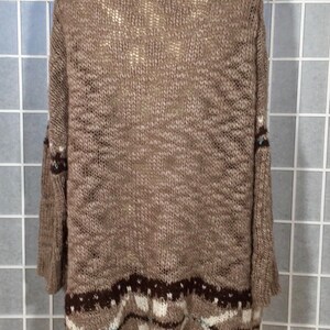 May include: A brown knit sweater with a wide neckline and three-quarter sleeves. The bottom hem features a geometric pattern in shades of brown, white, and blue. The sweater is displayed on a mannequin.