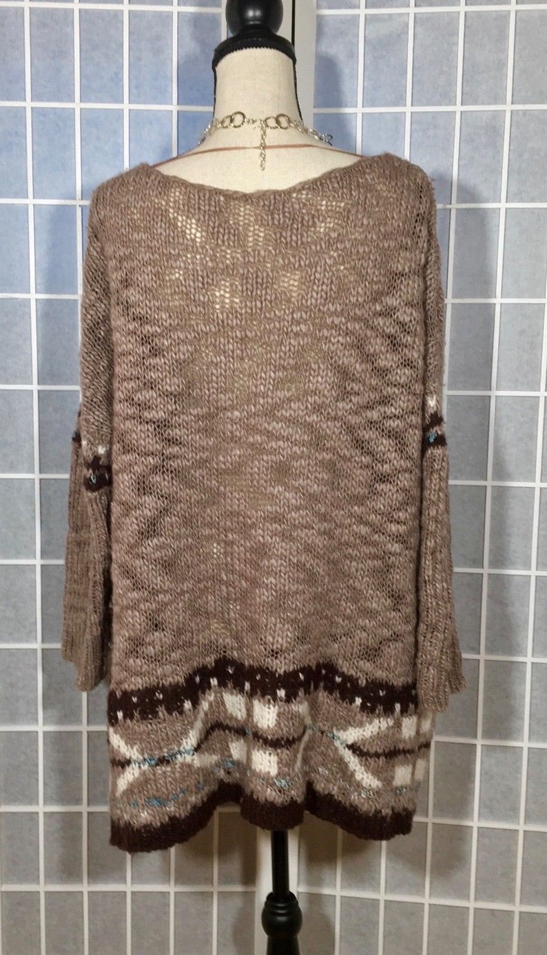 May include: A brown knit sweater with a wide neckline and three-quarter sleeves. The bottom hem features a geometric pattern in shades of brown, white, and blue. The sweater is displayed on a mannequin.