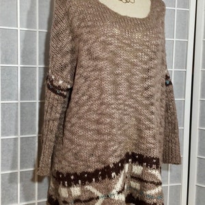 May include: A brown knit sweater with a scoop neck and long sleeves. The sweater features a patterned design in shades of brown, white, and teal at the hem and cuffs. A gold-colored necklace is visible around the mannequin's neck.