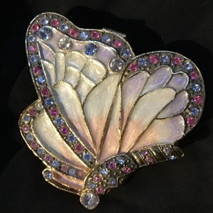 May include: A gold-tone butterfly-shaped trinket box with a white and pink enamel finish. The box is decorated with blue and pink rhinestones.