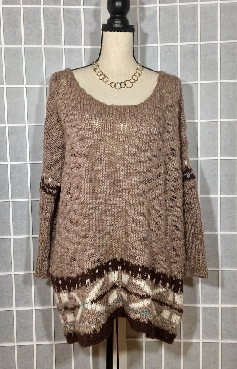 May include: A brown knit sweater with a scoop neck and long sleeves. The sweater has a patterned design at the bottom in shades of brown, white, and teal. A gold-colored chain necklace is around the mannequin's neck.