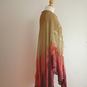 Puede incluir: Un poncho largo y fluido de punto degradado con un dobladillo con volantes. El poncho es una mezcla de colores verde, naranja y rojo.