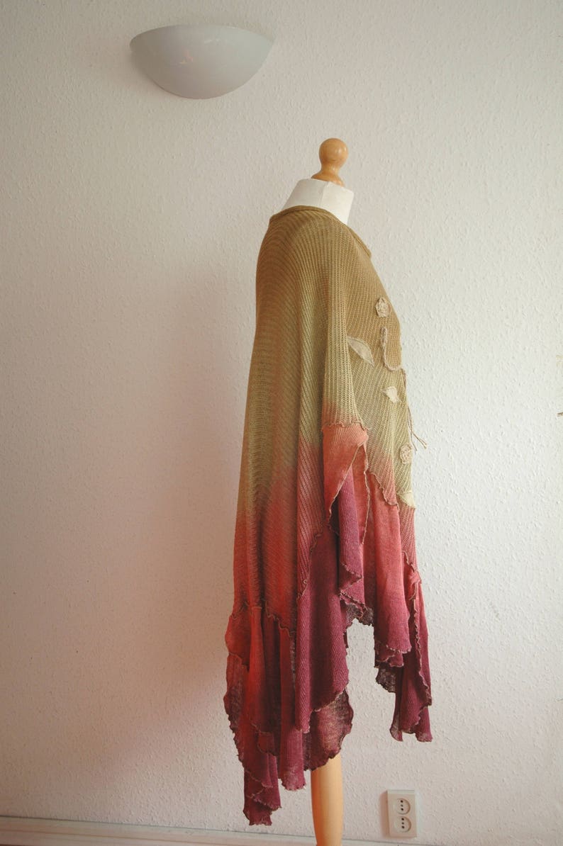 Puede incluir: Un poncho largo y fluido de punto degradado con un dobladillo con volantes. El poncho es una mezcla de colores verde, naranja y rojo.