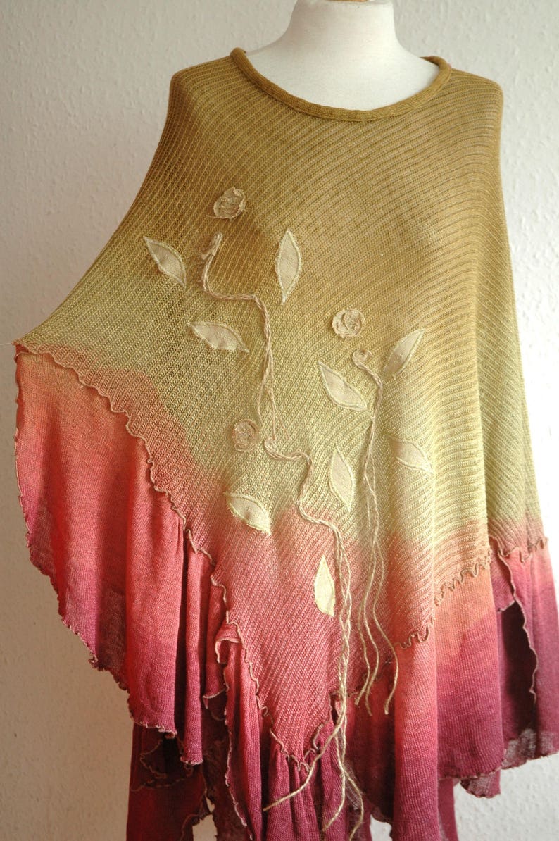 Puede incluir: Un poncho de punto con un degradado de amarillo, naranja y rojo. El poncho tiene un dise&ntilde;o floral con hojas y flores bordadas.
