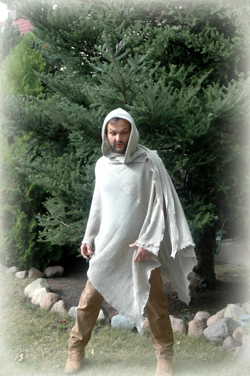 K&ouml;nnte beinhalten: Eine Person tr&auml;gt einen hellgrauen Kapuzenponcho mit einem langen, flie&szlig;enden Design. Der Poncho ist aus einem weichen, strukturierten Stoff gefertigt. Die Person steht vor einem gr&uuml;nen Baum.