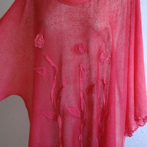 Puede incluir: Una blusa rosa transparente con detalles florales bordados. La blusa tiene un corte holgado y fluido y un escote redondo.