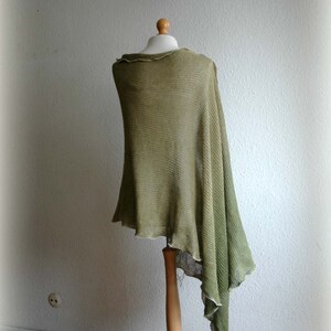 May include: A green knitted poncho draped over a wooden mannequin. The poncho has a loose, flowing fit and a fringed edge.