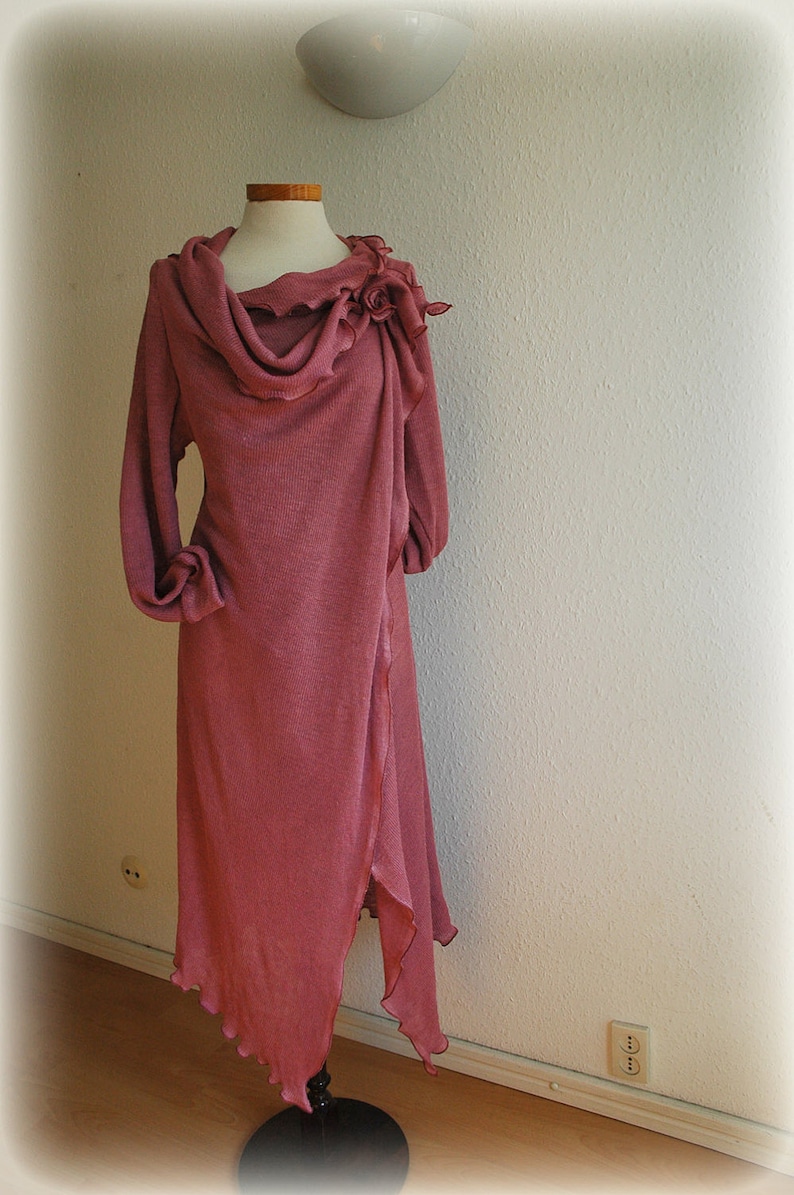 May include: A long, dusty rose colored, knitted wrap dress with a cowl neck and a flower detail on the shoulder.
