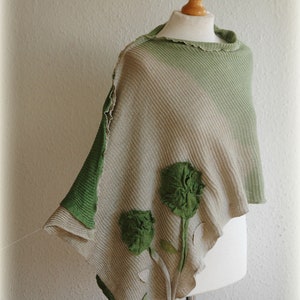 May include: A green and beige knitted poncho with a ruffled edge and green felt flower embellishments.
