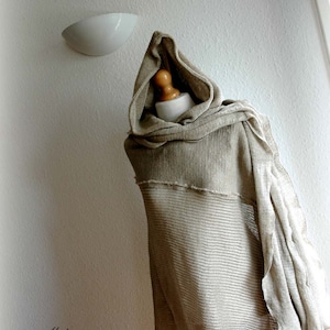 K&ouml;nnte beinhalten: Ein beiger Kapuzen-Linen-Schal mit einem strukturierten Strickmuster. Der Schal ist &uuml;ber eine Schaufensterpuppe gelegt.