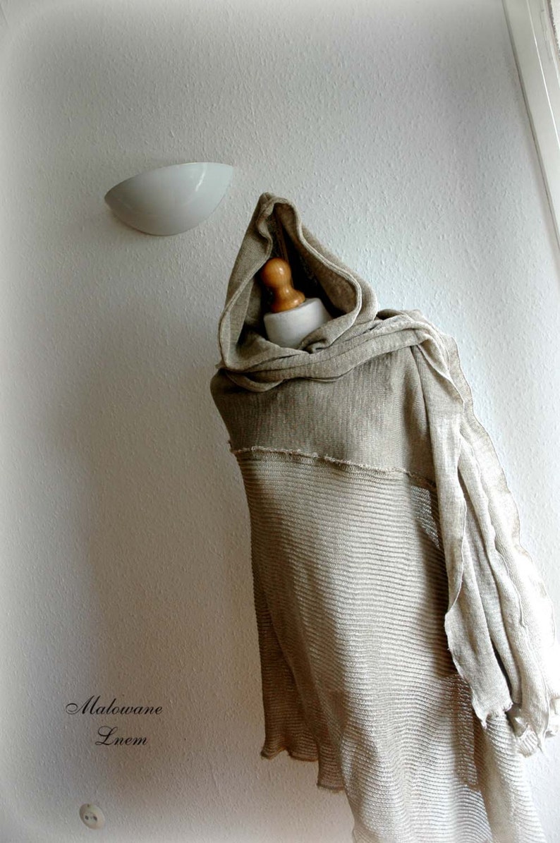 K&ouml;nnte beinhalten: Ein beiger Kapuzen-Linen-Schal mit einem strukturierten Strickmuster. Der Schal ist &uuml;ber eine Schaufensterpuppe gelegt.