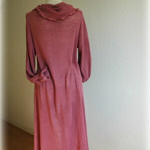 May include: A long-sleeved, pink, knitted dress with a cowl neck and a ruffled hem.