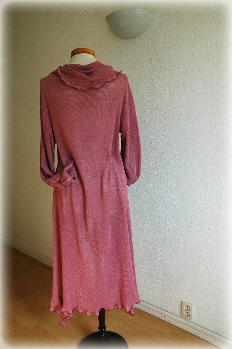 May include: A long-sleeved, pink, knitted dress with a cowl neck and a ruffled hem.